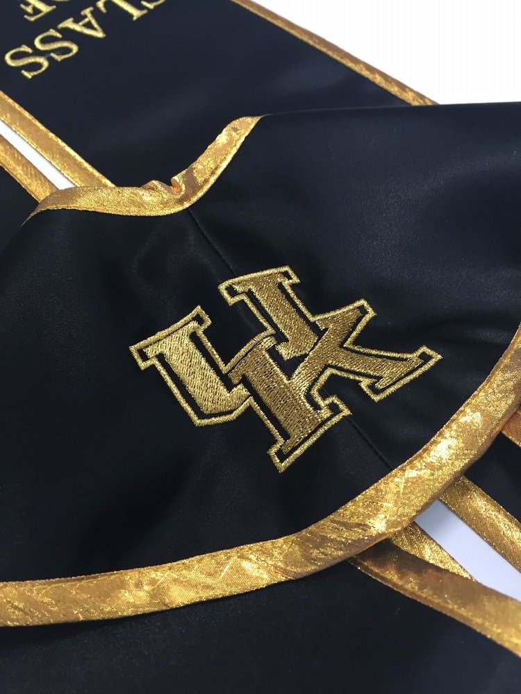 Red sash with embroidered black logo and white COLLEGE lettering, clamped in an embroidery machine