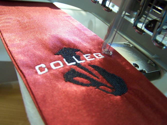 Stickmaschine bestickt rote Schärpe mit Hochschul-Logo in unserer Fertigung