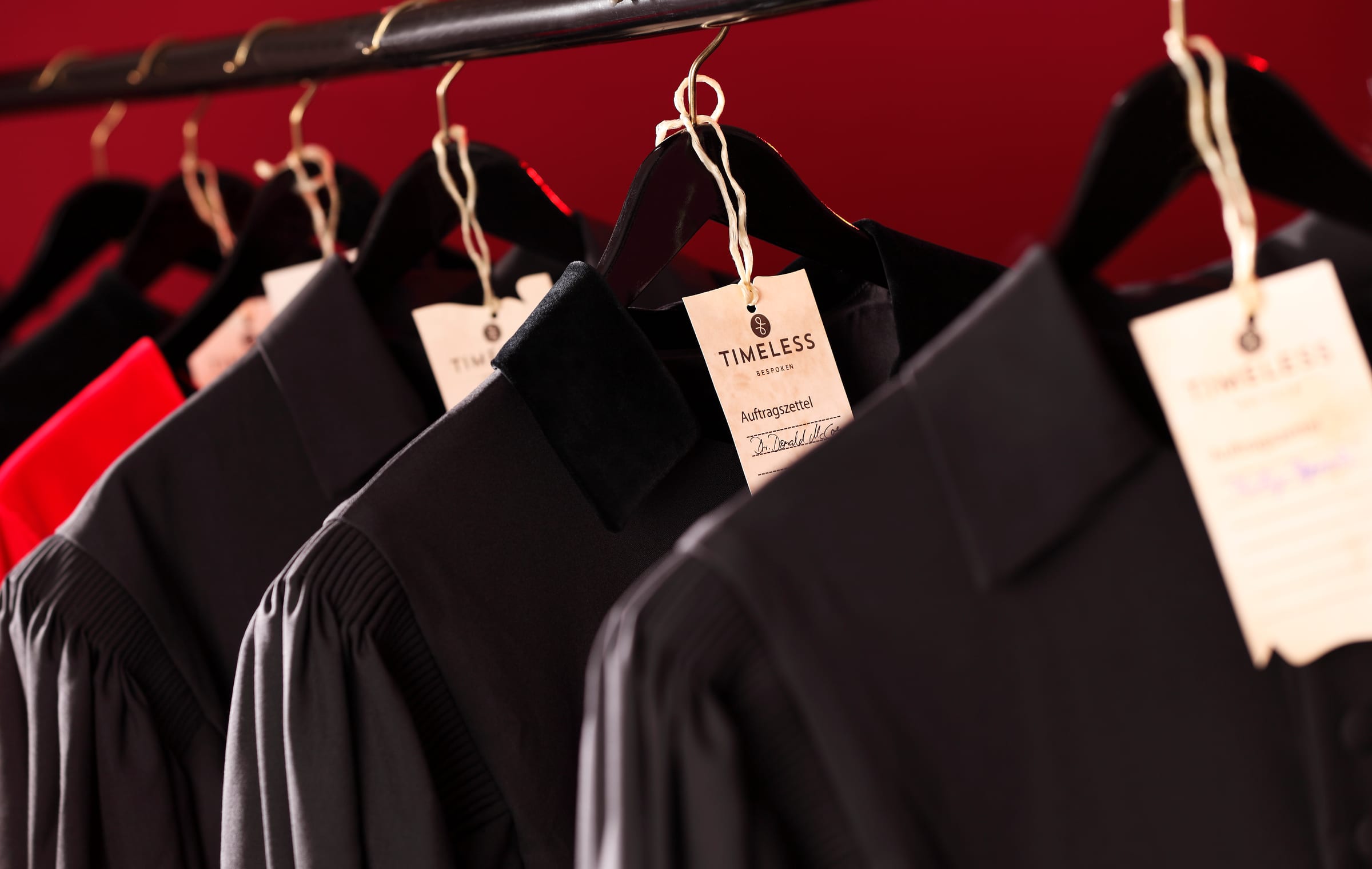 Handgefertigte schwarze Roben auf Kleiderbügeln im Atelier, mit Auftragszetteln versehen