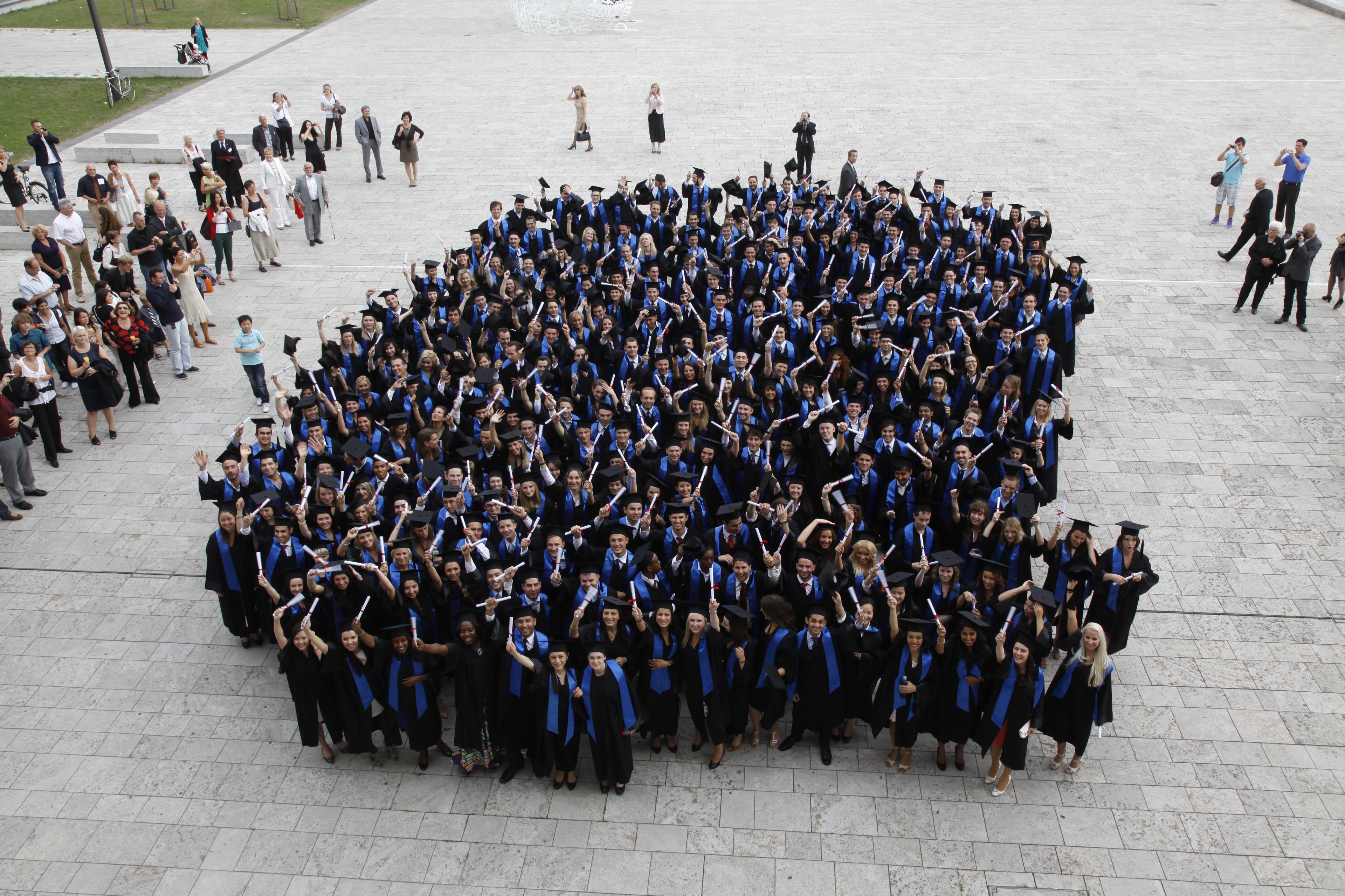 Graduates in gowns with golden sashes in front of a historic castle