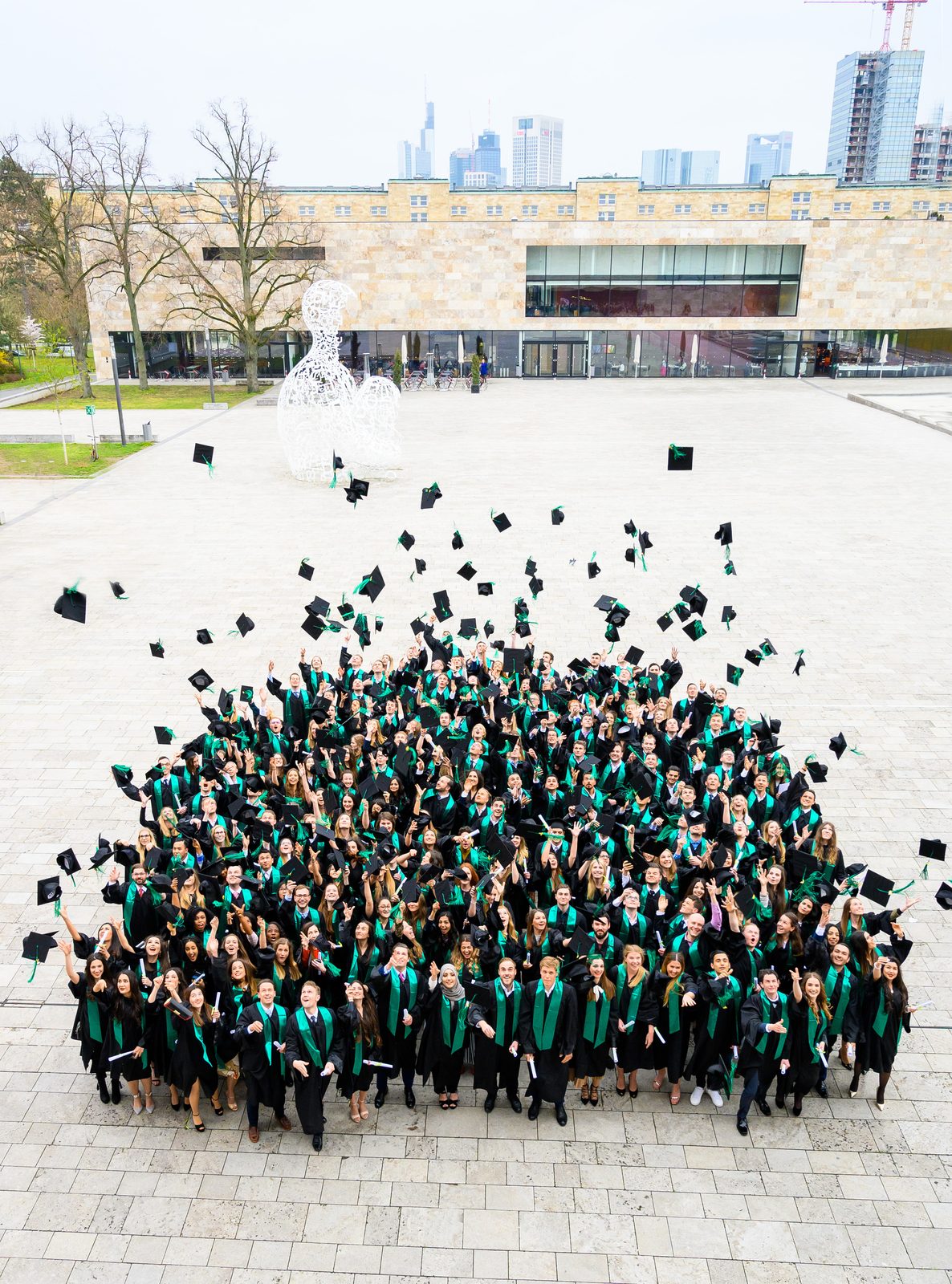 Graduates with green sashes in front of the Frankfurt skyline